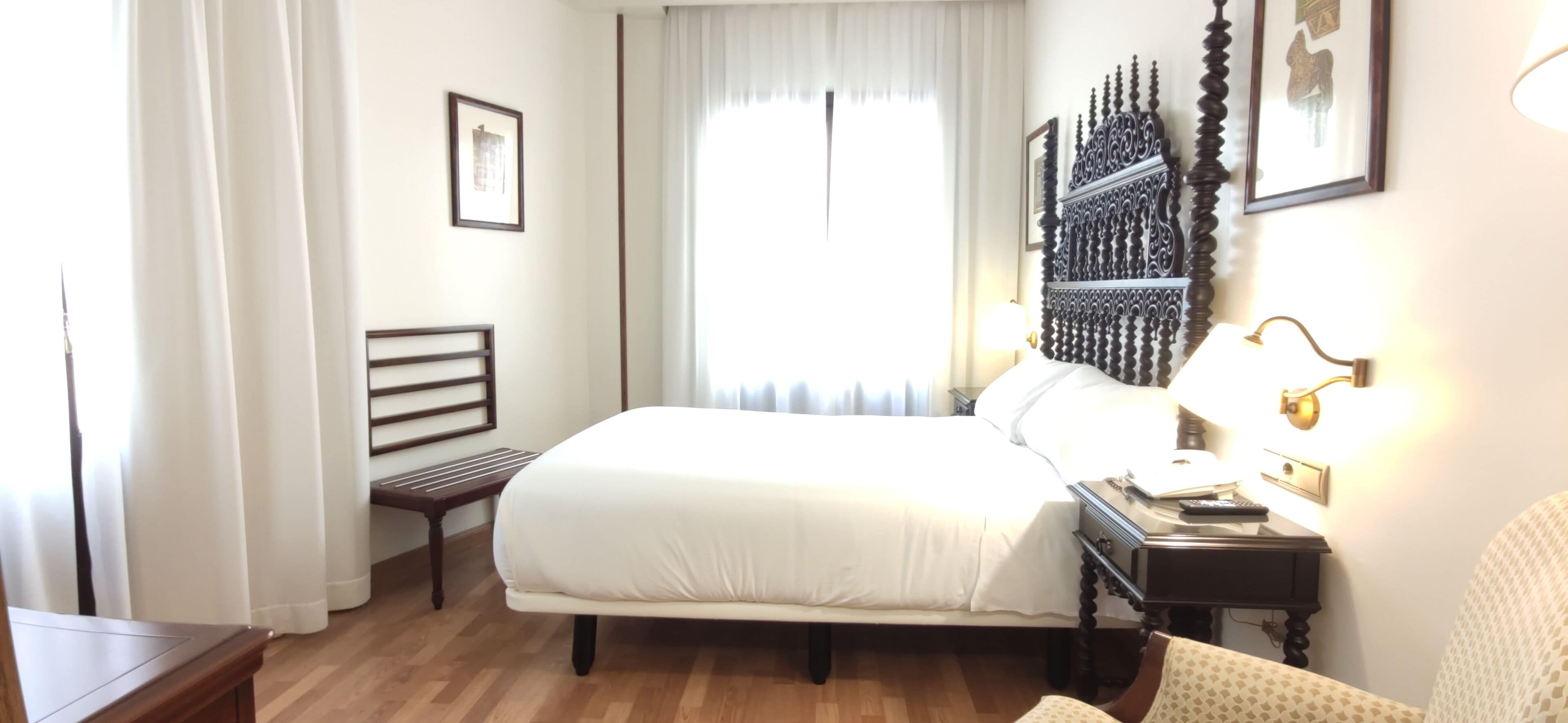 Una habitación de hotel con una cama, una mesita de noche, una lámpara y una silla.