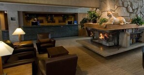 A lobby with a reception desk, leather seating, a fireplace, and a stone wall. - Lodge at Snowbird (Sandy)