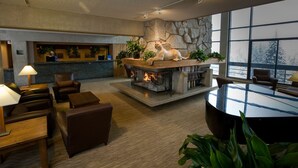 Un hall d’entrée moderne avec une cheminée en pierre, des sièges confortables et une grande fenêtre donnant sur la forêt.