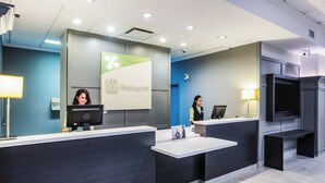 A reception desk with two employees, a digital display, and a sign indicating a holiday inn. - Holiday Inn & Suites Grande Prairie Conference Center by IHG (Grande Prairie)