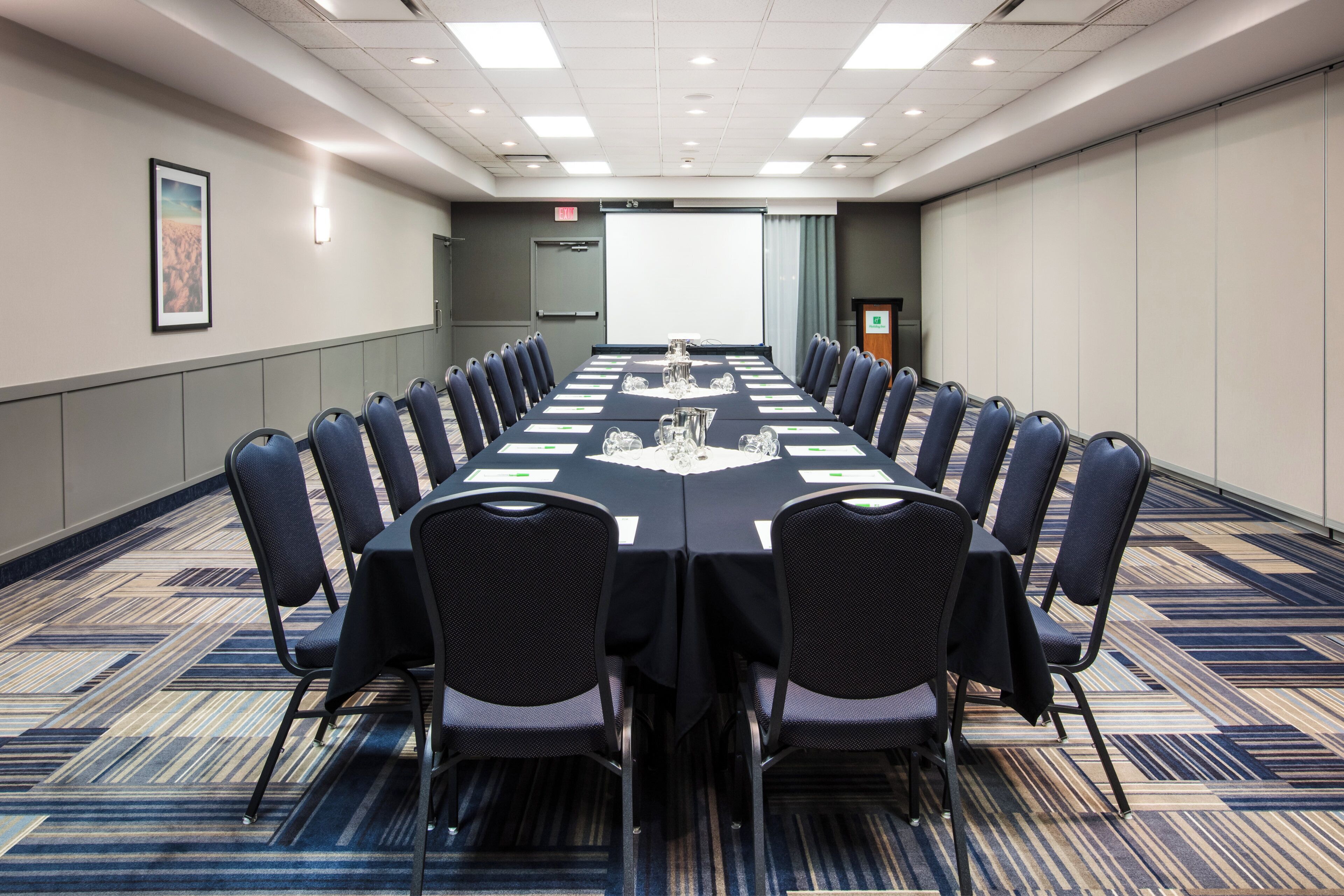 A conference room with a long table, chairs, and a projector screen.