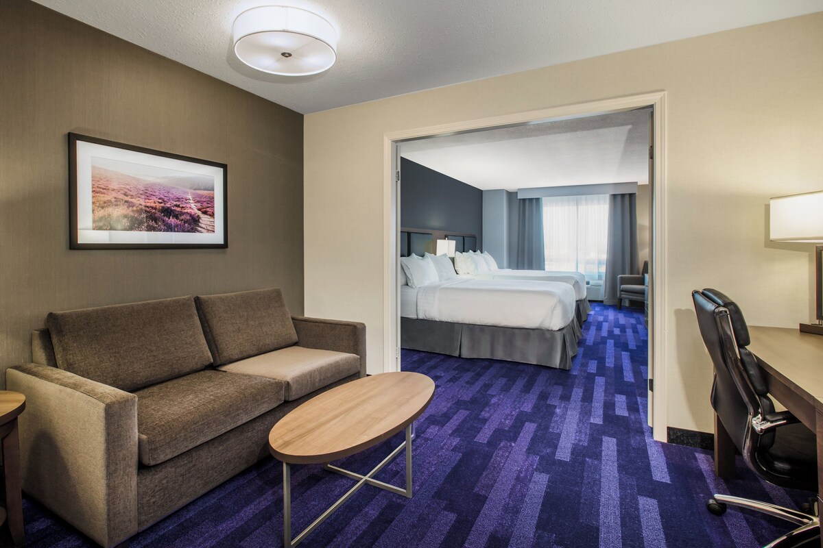A hotel room with a sofa, a small table, a bed, a desk, and a chair.