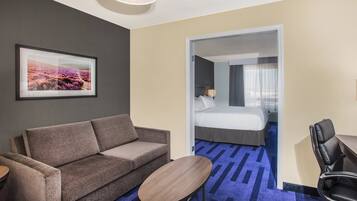 Een hotelkamer met een bank, een tafeltje, een bed met een witte dekbedovertrek, een lamp en een groot raam met gordijnen.