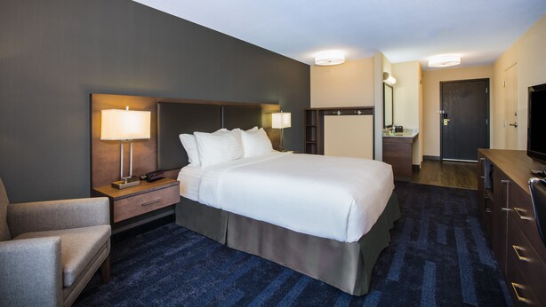 A hotel room with a large bed, bedside tables with lamps, a desk, a chair, a dresser, and a television. - Holiday Inn & Suites Grande Prairie Conference Center by IHG (Grande Prairie)