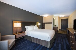 A hotel room with a large bed, bedside tables with lamps, a desk, a chair, a dresser, and a television.
