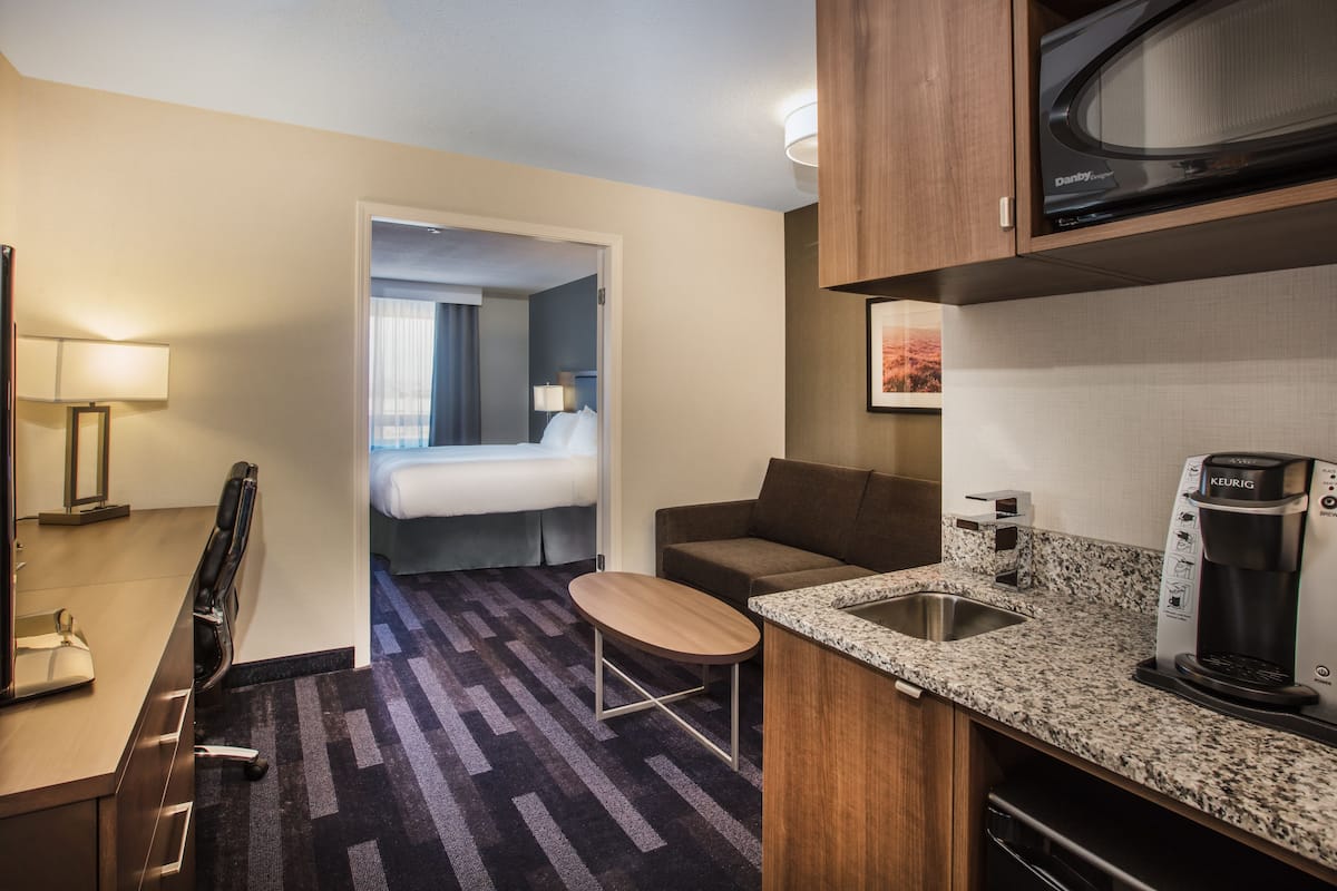 Una habitación de hotel compacta con kitchenette, una cama, una zona de estar y una puerta que da a un baño.