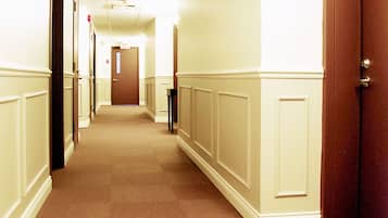 A hotel corridor with a carpeted floor, white walls, and a wooden door on the right.