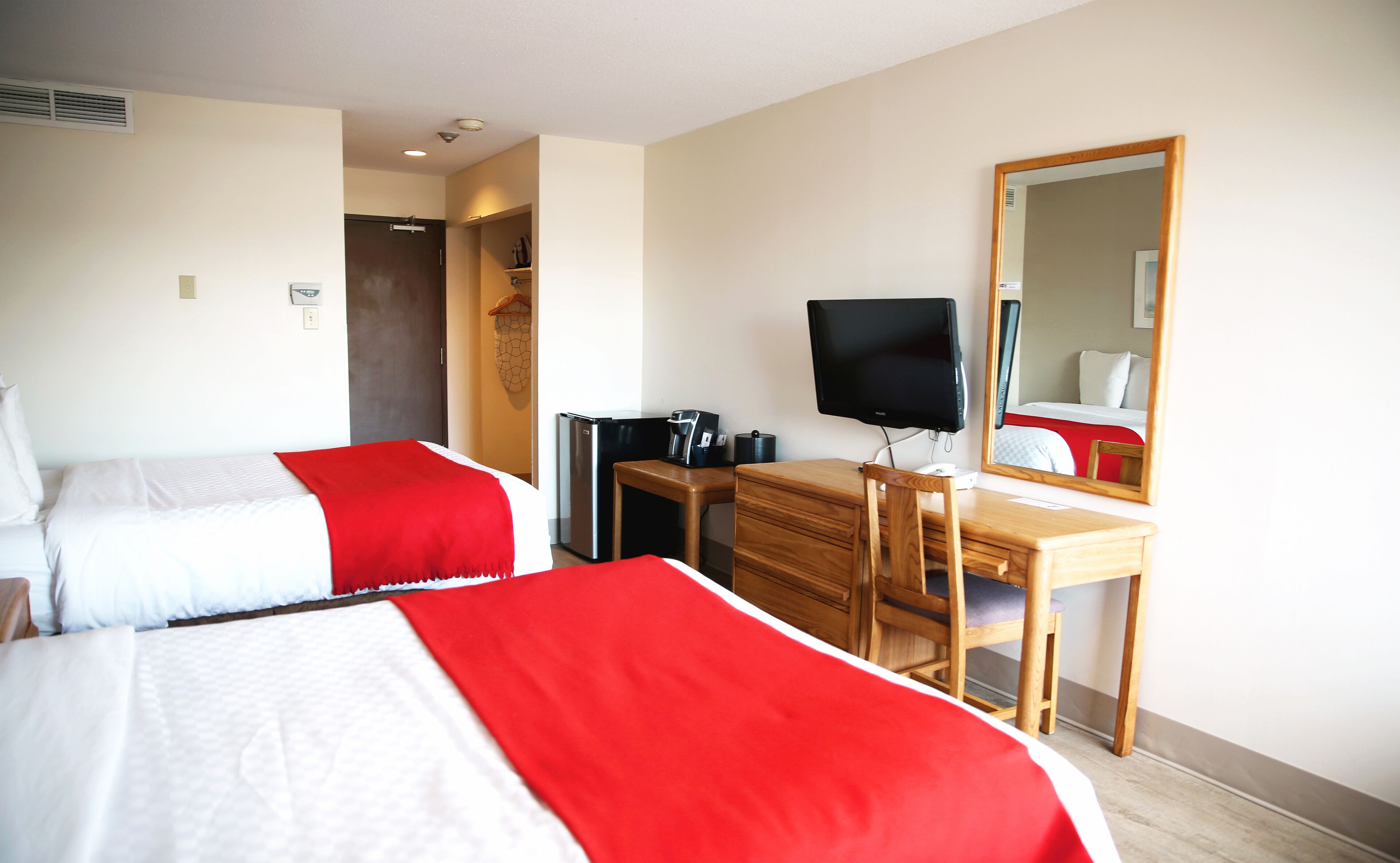 A hotel room with two beds, a desk, a television, and a mirror.