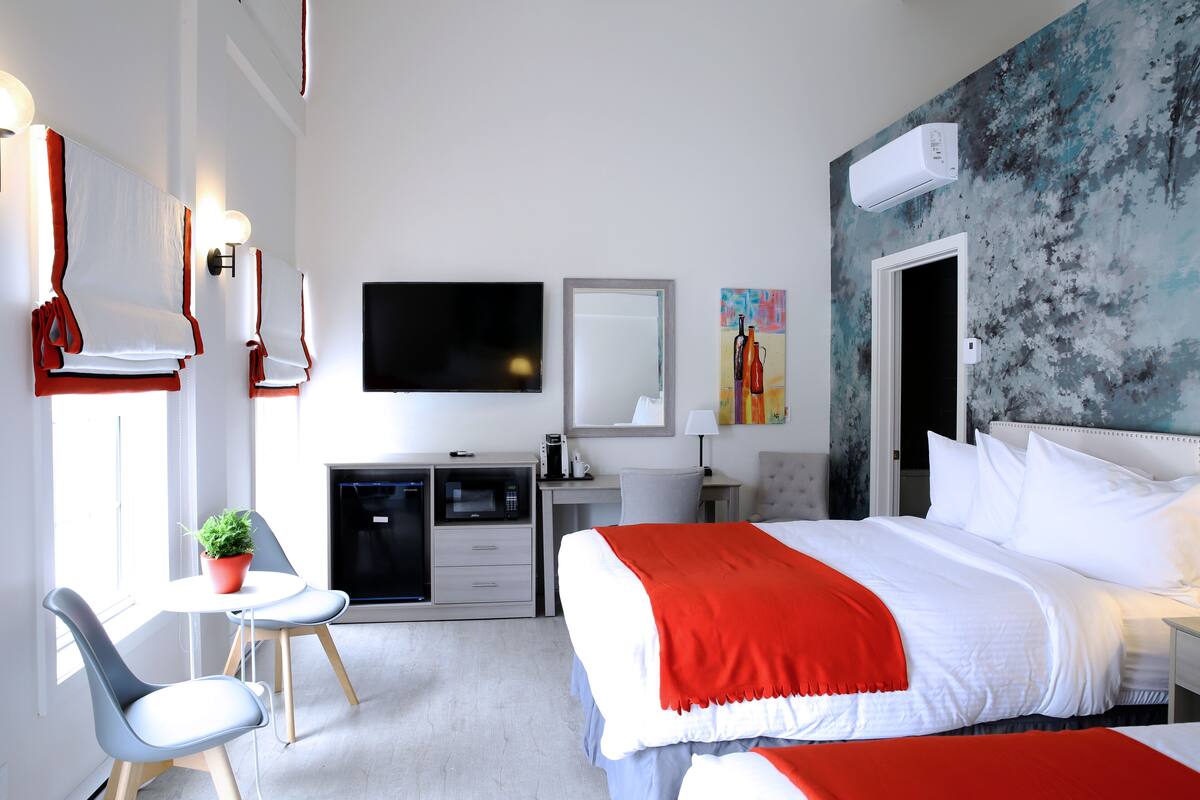 A modern hotel room with a large bed, a desk with a computer, a small table with a plant, and a TV on the wall.