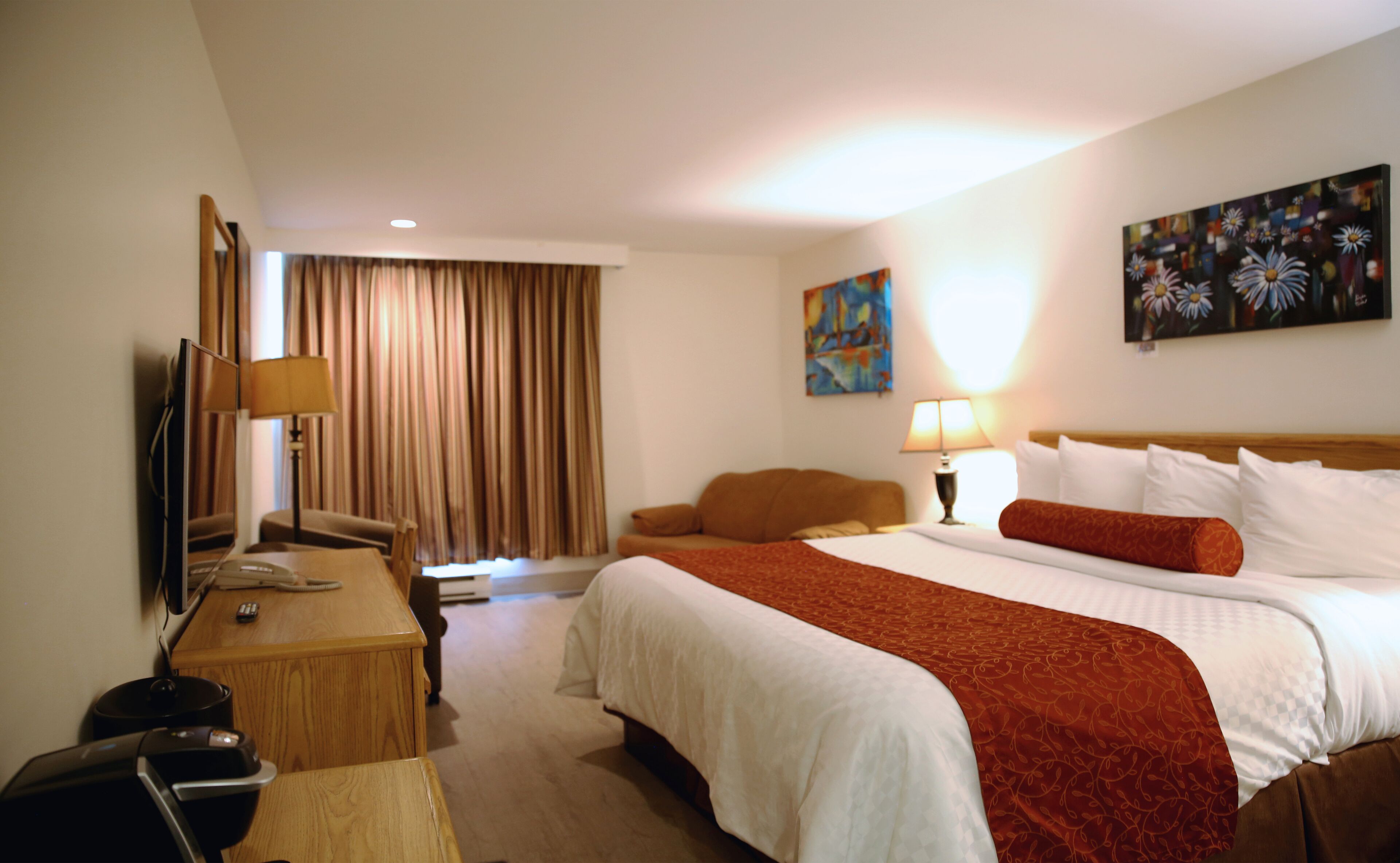 A hotel room with a large bed, a desk with a lamp, a TV, and a painting on the wall.