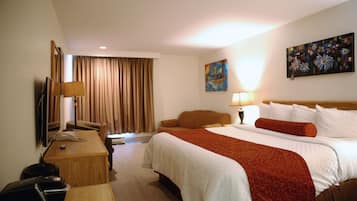 A hotel room with a large bed, a desk with a lamp, a TV, and a painting on the wall.