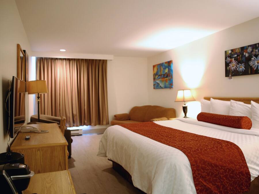A hotel room with a large bed, a desk with a lamp, a TV, and a painting on the wall.