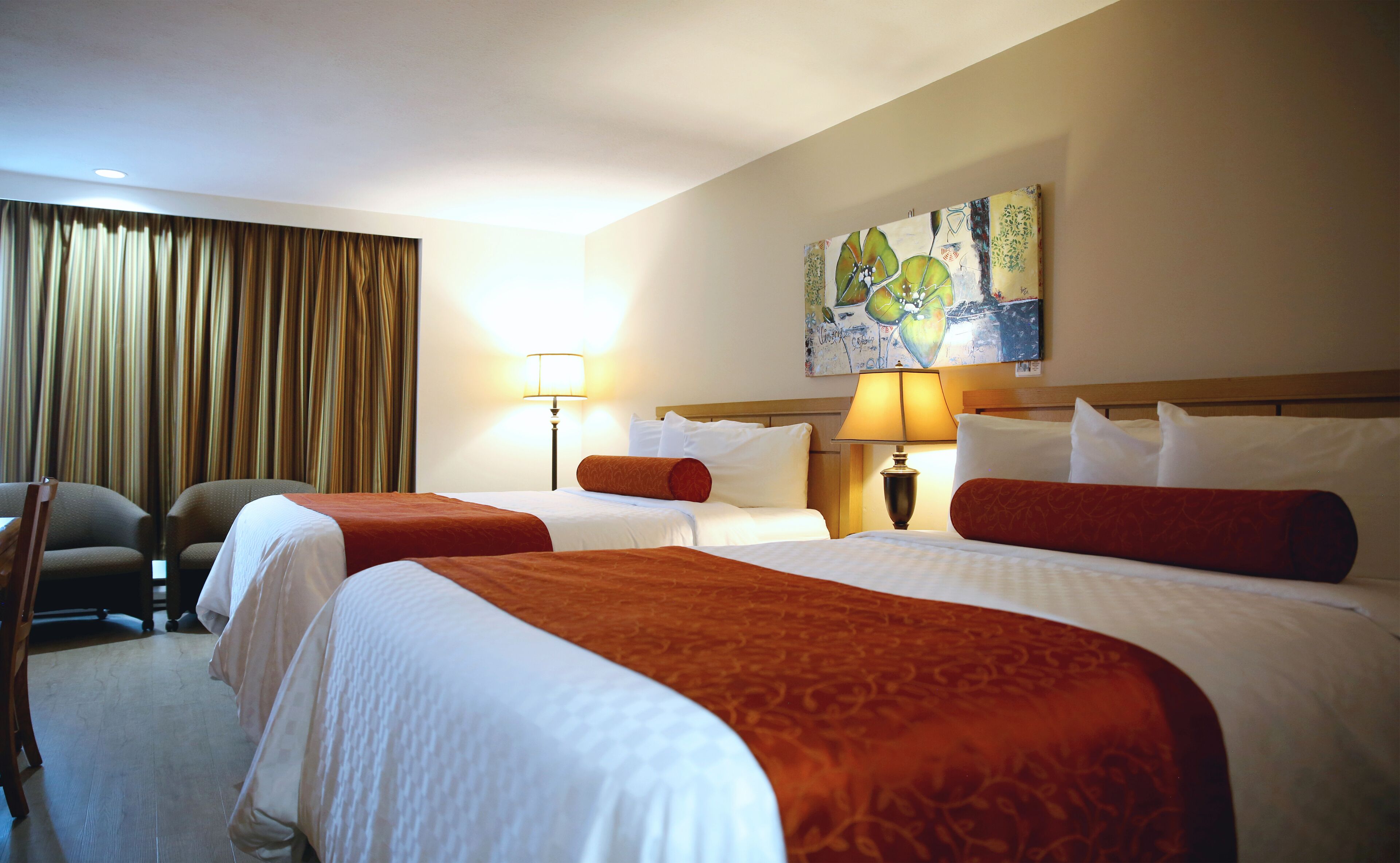 A hotel room with two beds, a large window with curtains, a painting on the wall, and a chair.