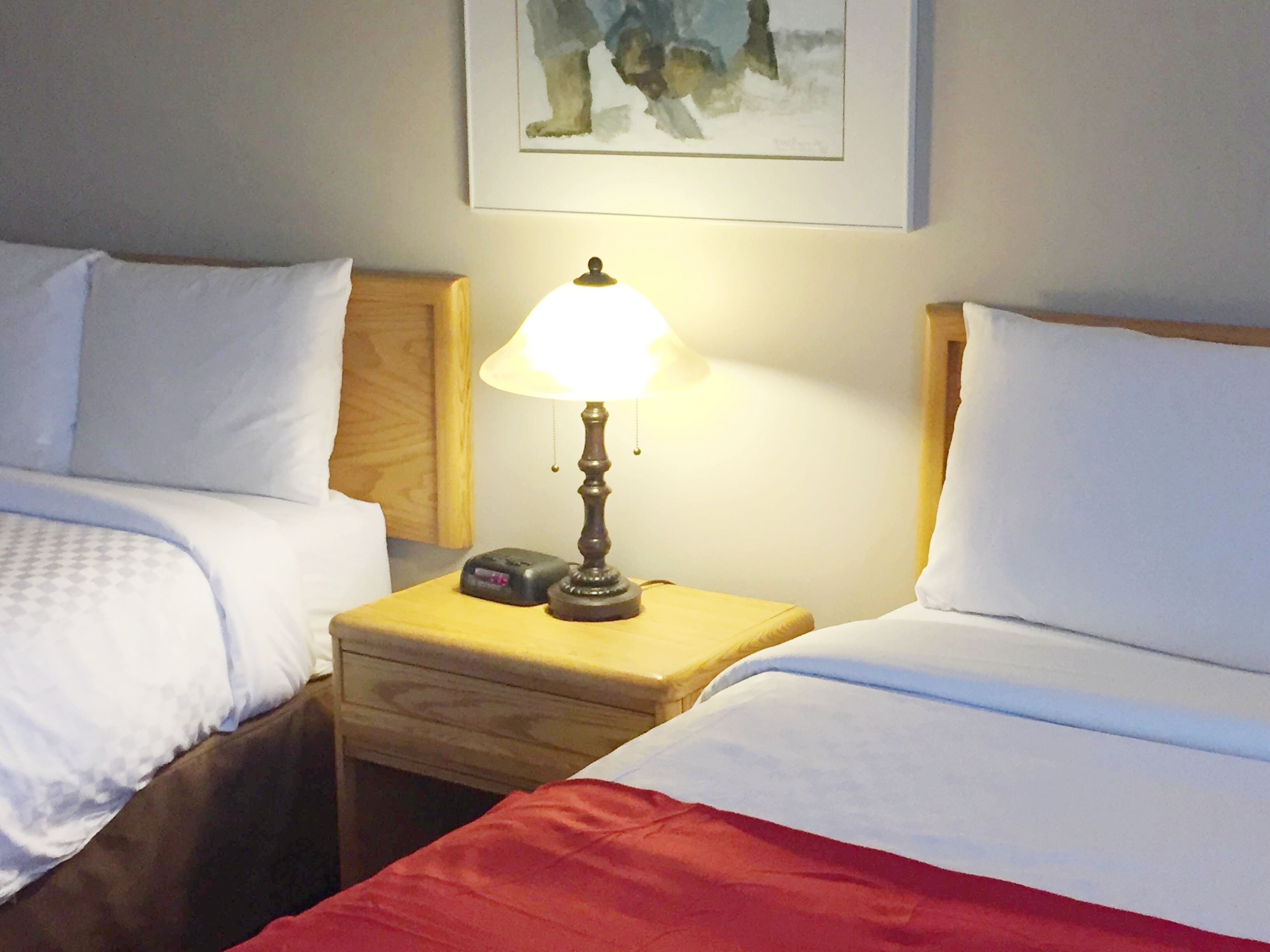 A hotel room with two beds, a nightstand with a lamp, and a painting on the wall.