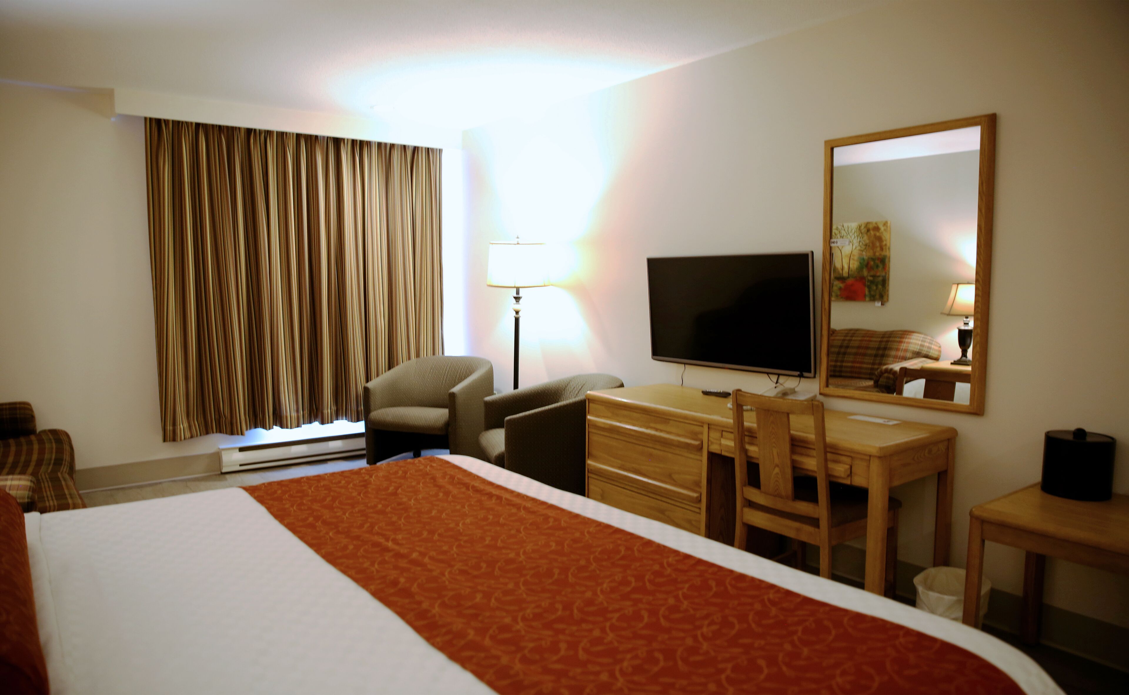 A hotel room with a bed, a desk, a chair, a television, a lamp, and a window with curtains.