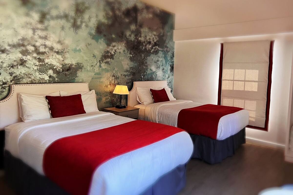 A hotel room with two beds, a large window, and a textured wall.