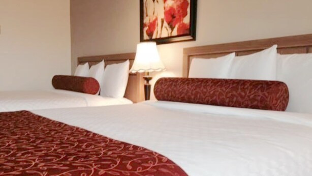 A hotel room with two beds, a red patterned bedspread, white pillows, and a floral artwork on the wall. - Auberge Du Grand Lac (Magog)