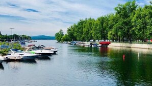 A calm lake with boats docked on the left, surrounded by lush green trees and a clear sky. - Auberge Du Grand Lac (Magog)