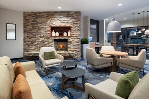 A modern living room with a stone fireplace, comfortable seating, and a dining area. - Fairfield Inn & Suites Orlando Ocoee (Ocoee)