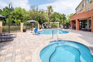 Ein Poolbereich mit Liegestühlen, Sonnenschirmen und einer gefliesten Terrasse.