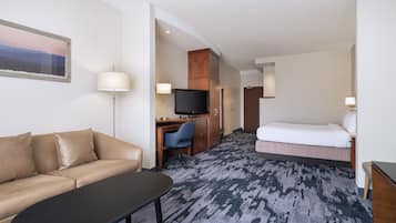 A hotel room with a sofa, a desk with a TV, a bed, and a carpeted floor.