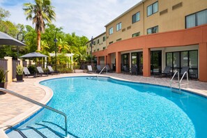 A swimming pool with lounge chairs and umbrellas, surrounded by a building with large windows and a brick pathway. - Fairfield Inn & Suites Orlando Ocoee (Ocoee)
