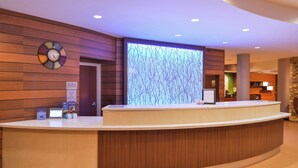 Zona de recepción de hotel con un mostrador de madera, un reloj digital y un cartel que indica 'No se admiten mascotas'.