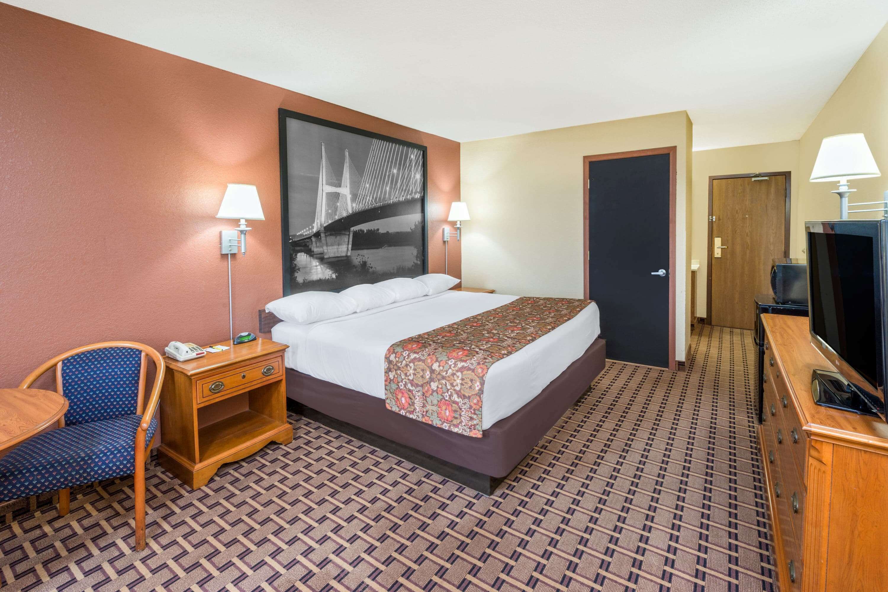 A hotel room with a bed, a desk, a chair, a TV, and a door.
