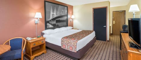 A hotel room with a bed, a desk, a chair, a TV, and a door.