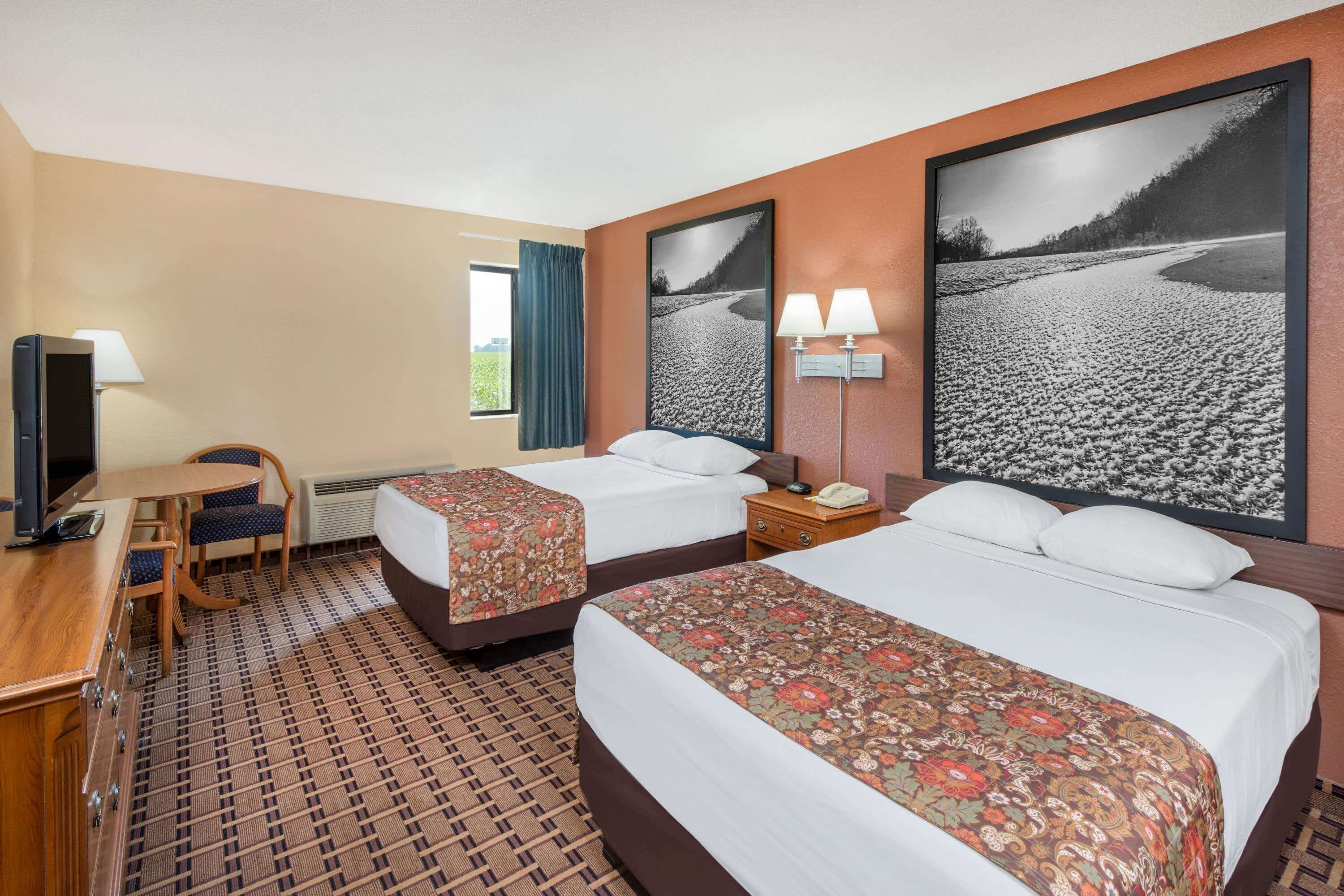 Quarto de hotel com duas camas, uma escrivaninha, uma cadeira, televisão e uma janela grande com cortinas.