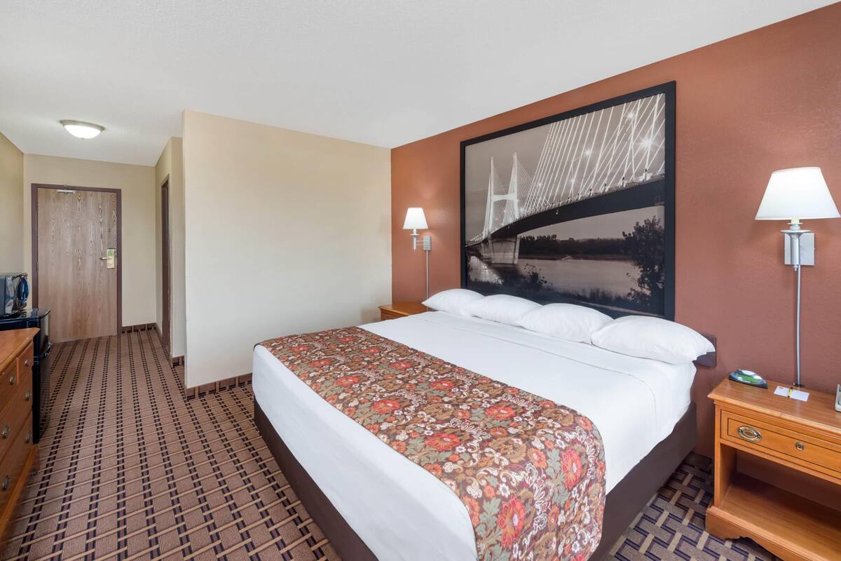 Ein Hotelzimmer mit einem großen Bett, zwei Nachttischlampen, einer Holzkommode und einem gemusterten Teppich.