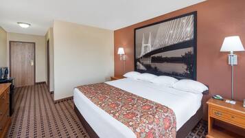A hotel room with a large bed, two bedside lamps, a wooden dresser, and a patterned carpet.