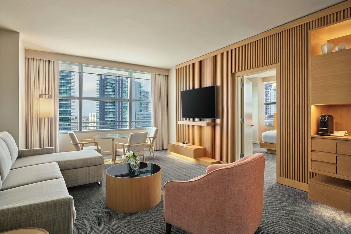Una habitación de hotel moderna con un ventanal grande, un televisor de pantalla plana, un sofá, una mesa de centro y una zona de escritorio.