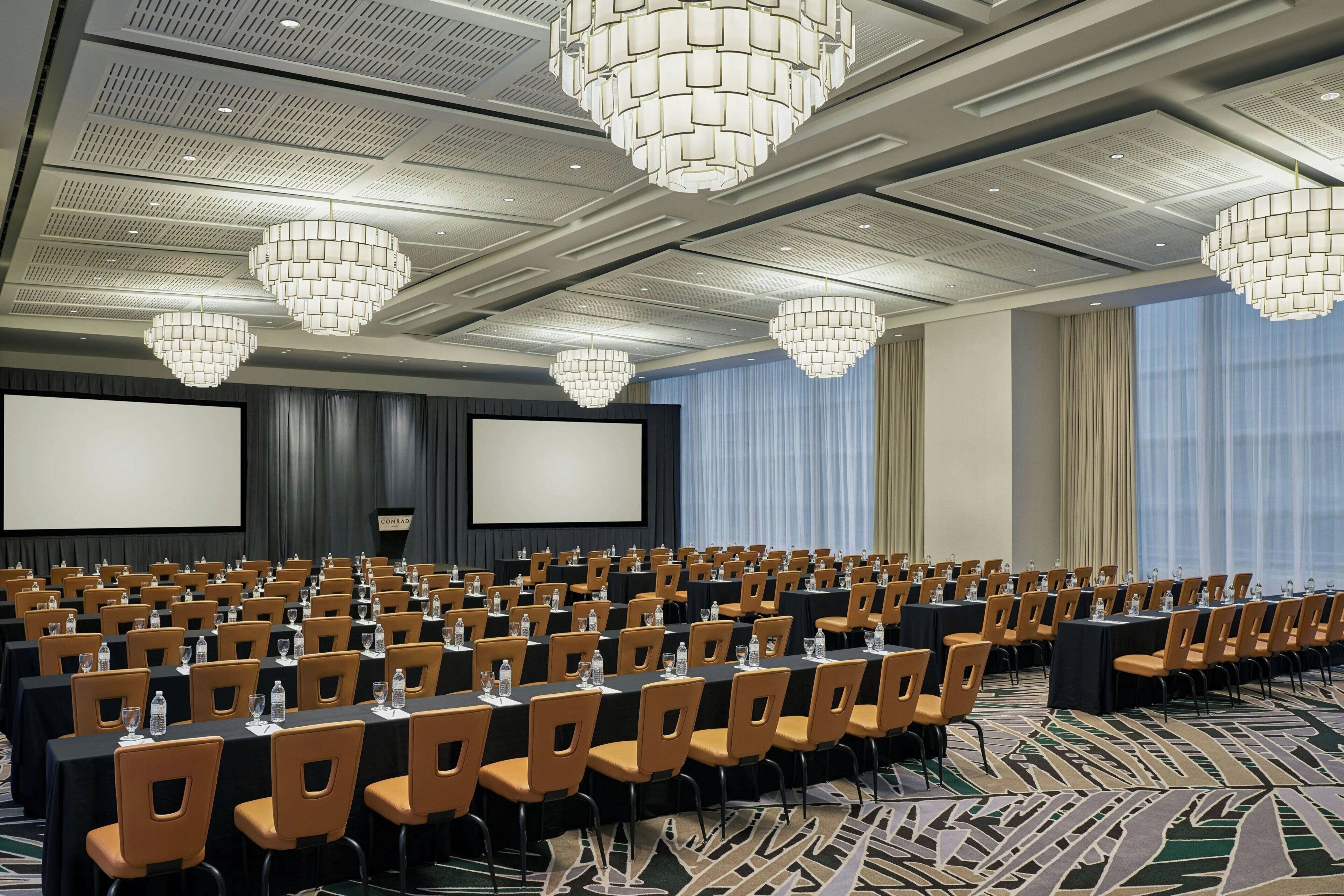 A conference room with rows of chairs, tables, and a large screen.