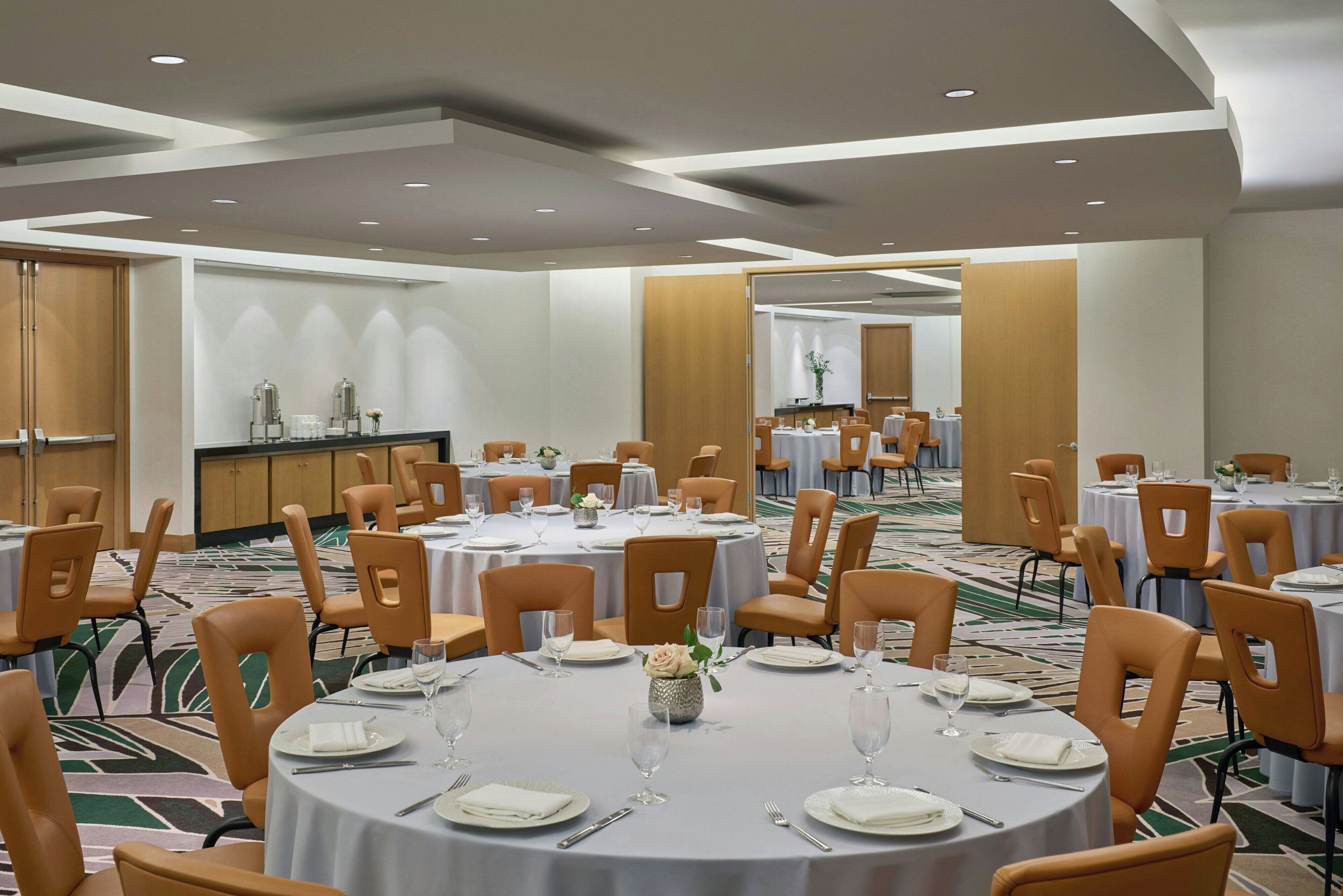 Une salle de conférence équipée de tables rondes, de chaises et d’un espace buffet.