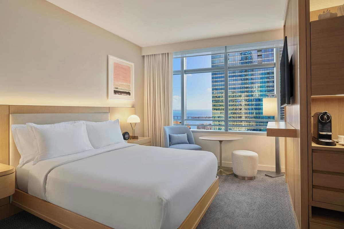 Habitación de hotel con una cama grande, un escritorio, una silla, un televisor y una ventana con vistas a la ciudad.