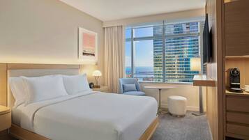 A hotel room with a large bed, a desk, a chair, a TV, and a window with a city view.