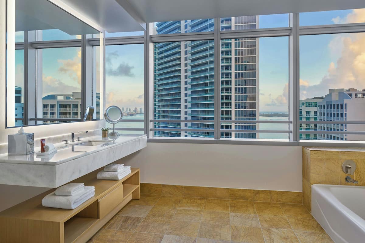 A modern bathroom with a large window, a bathtub, and a vanity with a mirror.