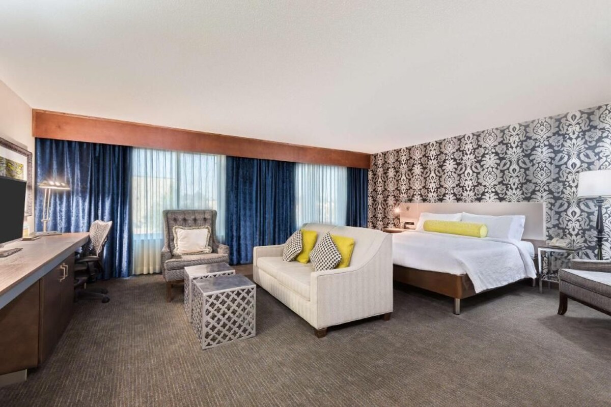 A hotel room with a bed, a sofa, a desk, and a chair.