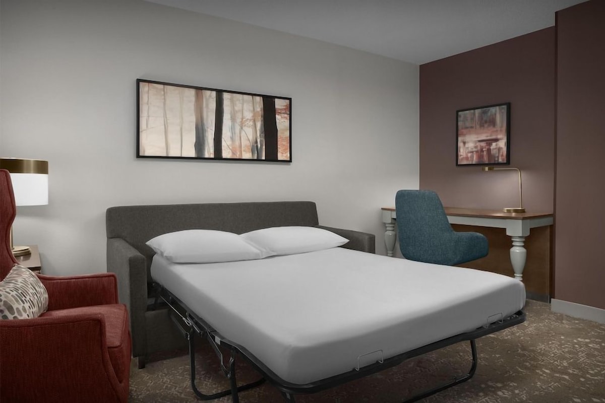 Habitación de hotel con una cama individual, un escritorio, una silla y dos obras de arte colgadas en la pared.
