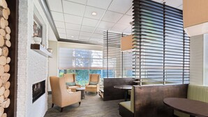 A modern lounge area with a fireplace, comfortable seating, and large windows offering views. - Hilton Garden Inn Westbury (Westbury)