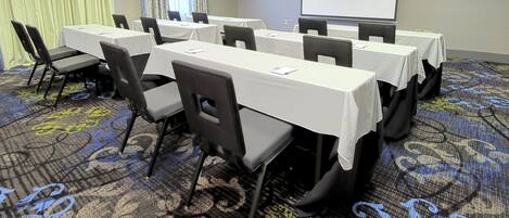 A conference room with tables and chairs, a projector screen, and a large window with curtains.