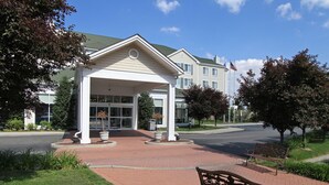 A covered entrance with a bench, a building with a flag, and a landscaped area. - Hilton Garden Inn Westbury (Westbury)