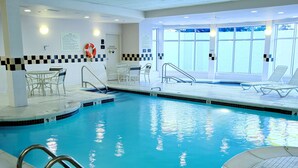 An indoor swimming pool with clear water, a lifebuoy, and a poolside area with chairs and tables. - Hilton Garden Inn Westbury (Westbury)
