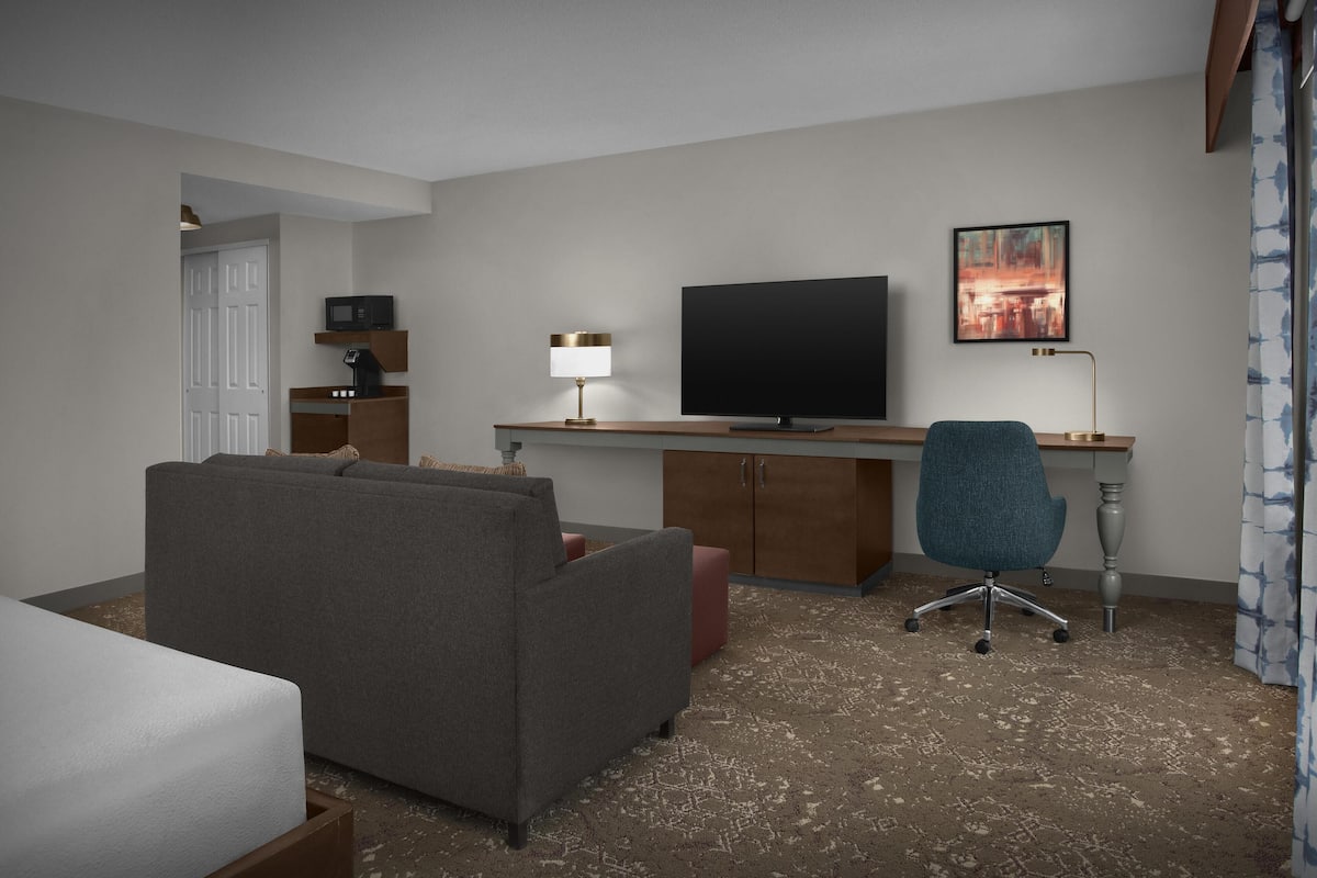Ett hotellrum med en soffa, ett skrivbord med en dator, en tv och en stol.