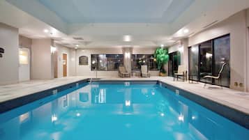 A large indoor swimming pool with clear blue water, surrounded by lounge chairs and a potted plant.