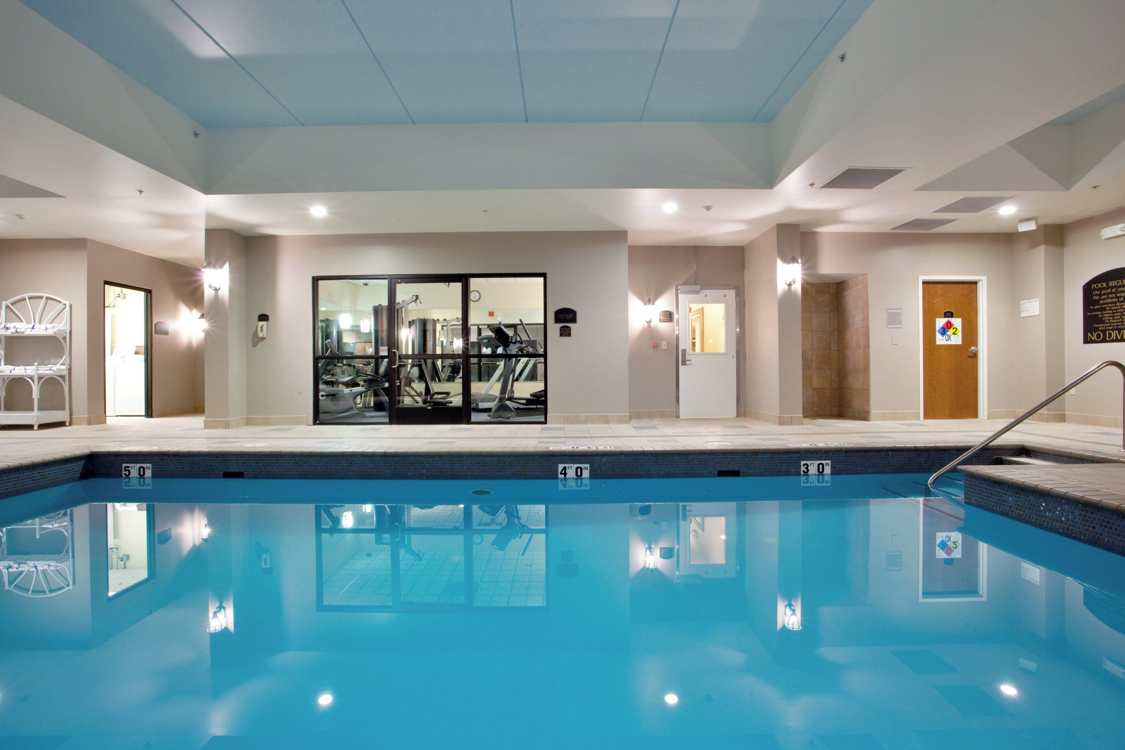 Una piscina con agua cristalina, rodeada por un área de gimnasio con equipo de ejercicio.