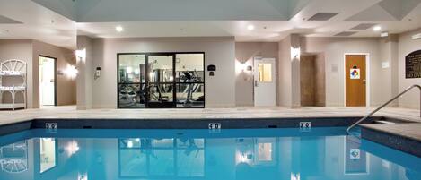 A swimming pool with clear water, surrounded by a gym area with exercise equipment.