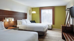 A hotel room with two beds, a wooden headboard, a desk with a lamp, a TV, and a window with blinds. - Holiday Inn Express & Suites Newport News by IHG (Newport News)