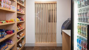 A snack and drink vending area with shelves stocked with various snacks and a refrigerated section with bottled drinks. - Holiday Inn Express & Suites Newport News by IHG (Newport News)